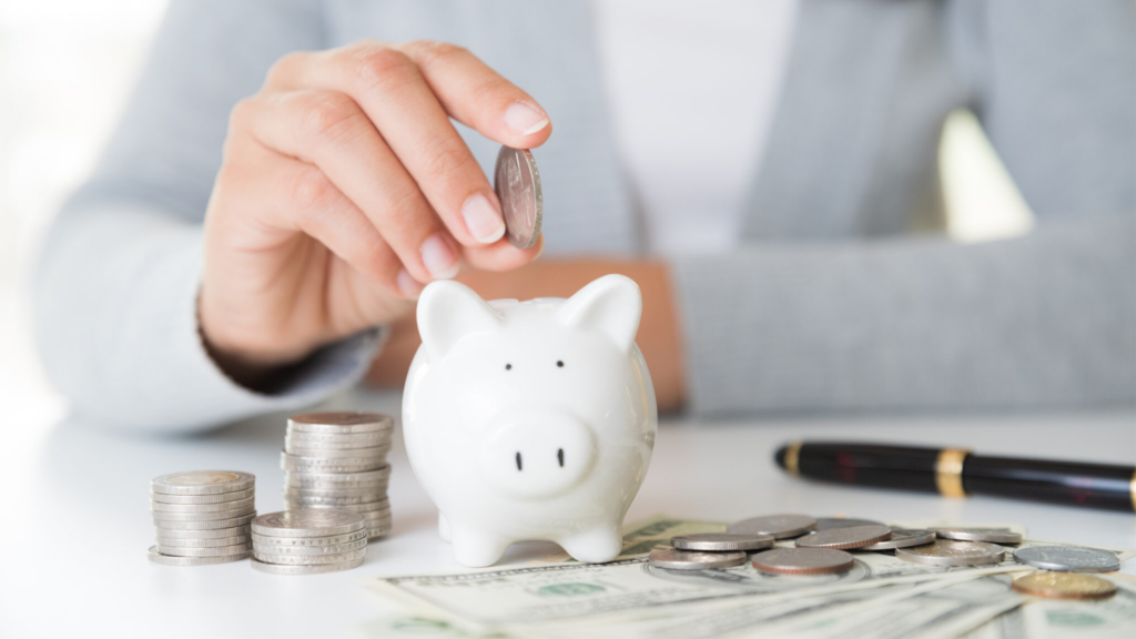 Woman hand putting money coin into piggy bank with stack of coin